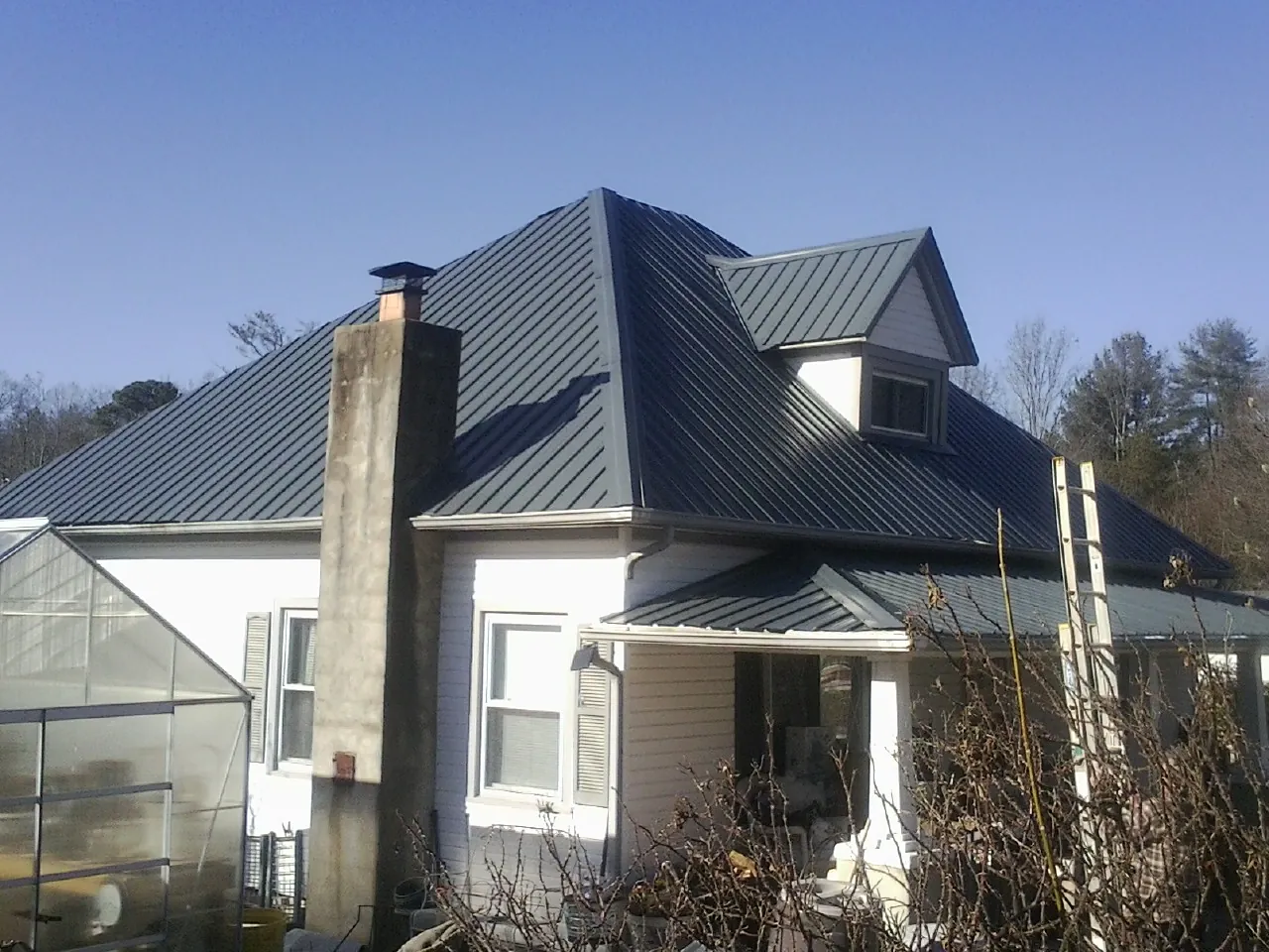 Dark blue standing seam metal roof on a white farmhouse with dormer — Slate & Tile Roof Repair by Roofing Brothers in Homewood
