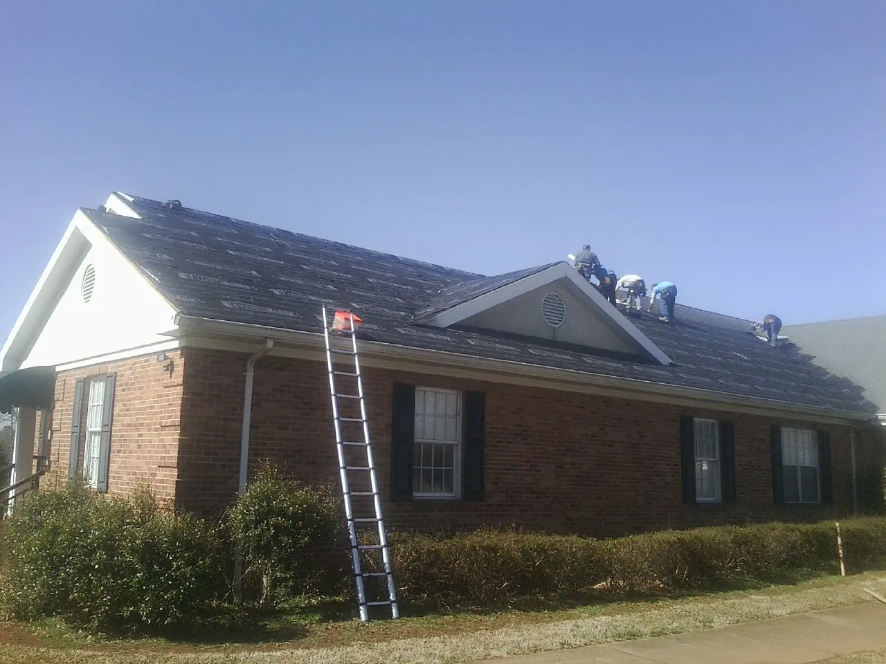 Crew tearing shingles off a brick ranch roof with a ladder set — Metal Roof Repair work by our crew in Homewood