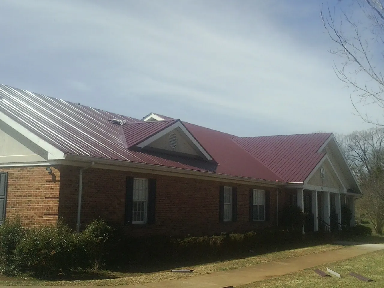 Red metal roof with gabled entries on a long brick building, from a Hail Damage Roof Repair job in Homewood