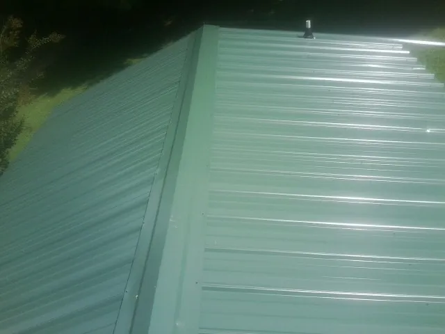 New green metal panels meeting at the ridge of a roof — Flat Roof Repair work by our crew in Homewood