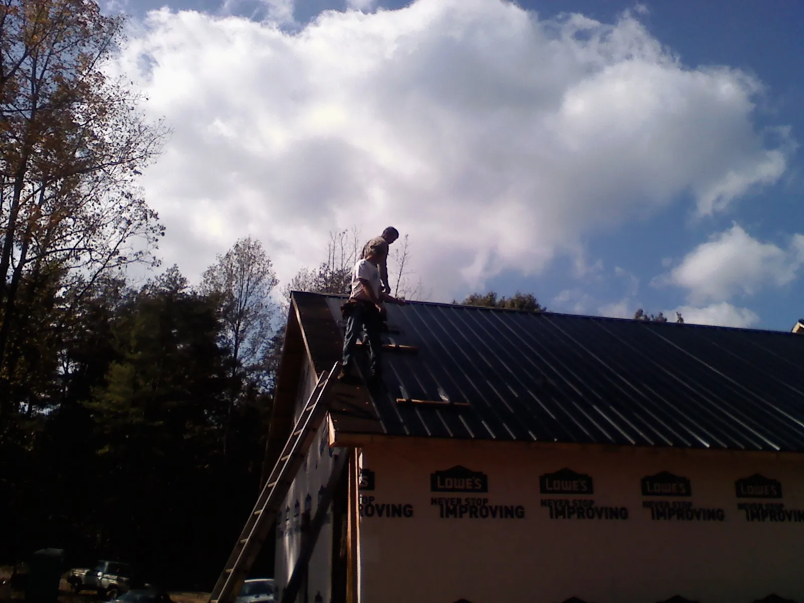 Roofer fastening dark metal panels high against a cloudy sky, from a Roof Inspection job in Homewood