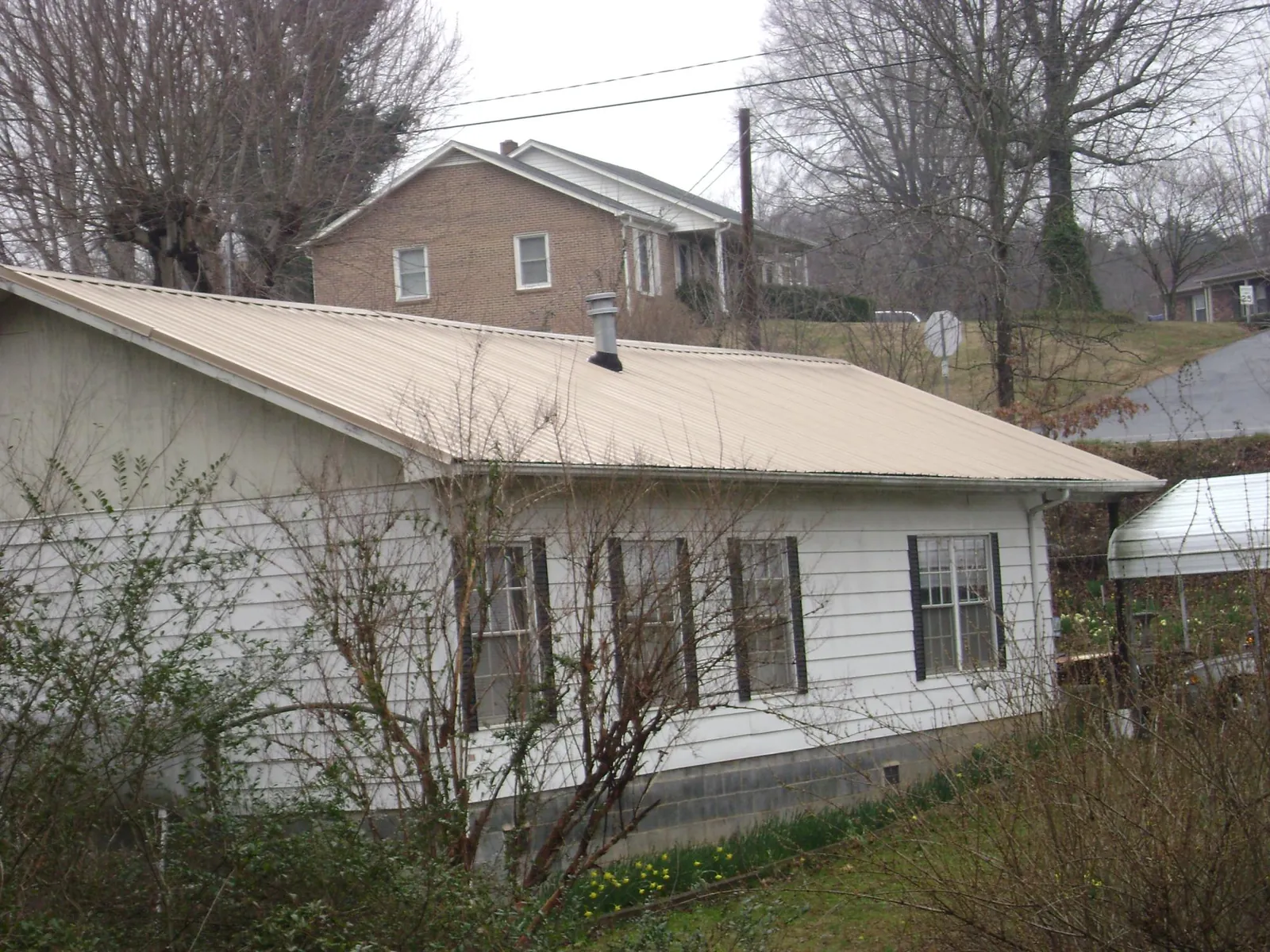 Tan metal roof on a white sided house set into a hillside — Commercial Roofing by Roofing Brothers in Homewood