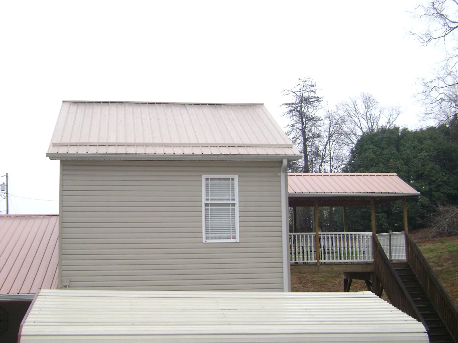 Tan metal roofs on a two story addition and attached porch, from a Roof Replacement job in Homewood